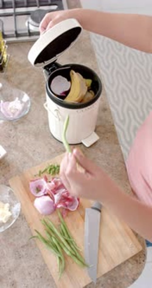 Vertical video of plus size woman composting vegetable waste in kitchen, slow motion