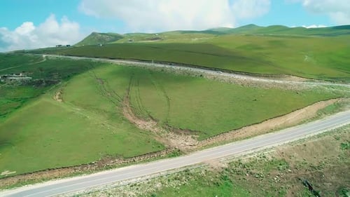 Aerial Over a Car Driving Along Winding Asphalt Road Among Mountains Covered with Green Grass in
