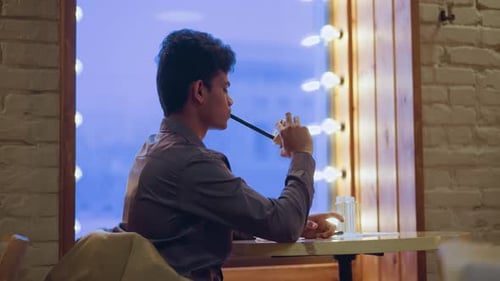 Young Man Wearing Gray Shirt Sitting By Window with Soft Glowing Lights