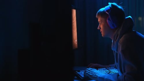 Seitenansicht eines fokussierten Spielers mit Gaming-Headset, der auf einem Stuhl sitzt und auf Tastatur und Maus klickt