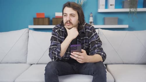 Man Sits with Phone on Couch at Home