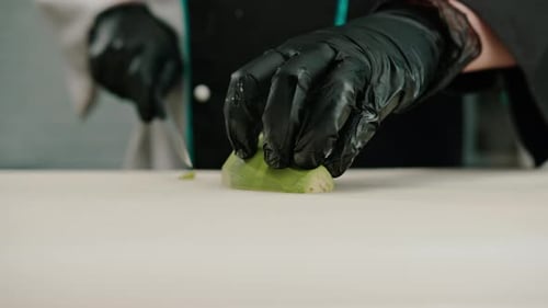 Close-up of a sushi maker in gloves cutting avocado with a professional kitchen knife on a board