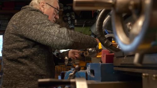 Mature man mechanical engineer working on lathe in workshop.