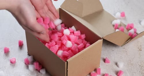 Femme mettant des morceaux de polystyrène dans une boîte en carton à une table gris clair, gros plan