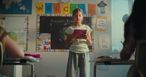 Smart Primary School Girl with Notebook Showcasing Knowledge of Ecology in Front of Class and