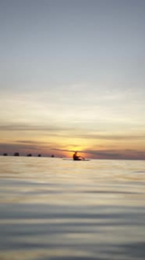 Two Adults Paddling in the Background at Sunset in the Sea