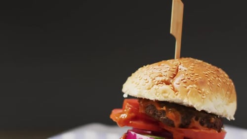 Video close up of cheeseburger in burger bun with wooden skewer, on grey background with copy space