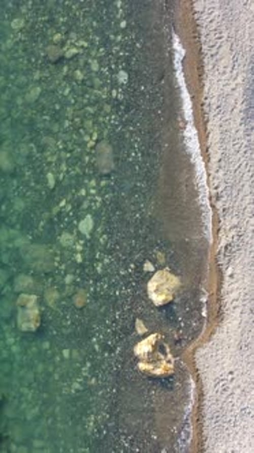 Aerial Vertical View of Beach with Wave Caressing Shore Sun Glare Small Waves on the Water Surface