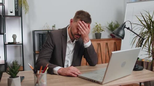 Tired Businessman Sits at Desk with Laptop