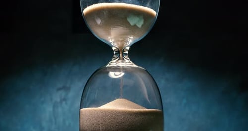 Hourglass with grains of sand on a dark background. Shot on super slow motion camera 1000 fps.