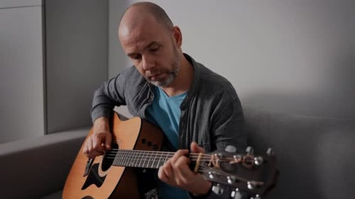 Man Plays Acoustic Guitar on Couch at Home