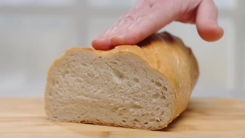 Fresh wheat bread on wooden board close-up. Female hand pressing on loaf of white bread