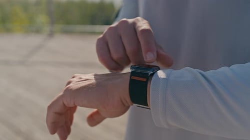 Man uses smartwatch technology outdoors during daytime.