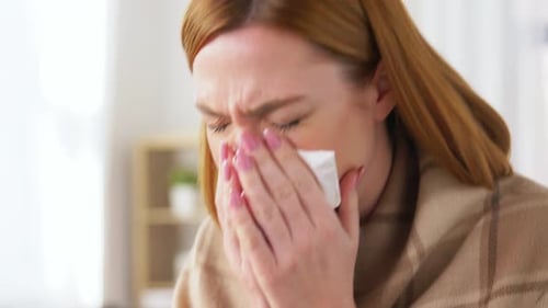Sick Woman Blowing Nose in Tissue at Home