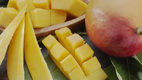Ripe mango fruits with slices and mango leaves.