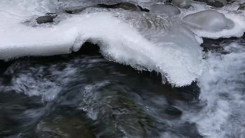 Gros plan d'une rivière à débit rapide et de rochers recouverts de glace. Début du printemps.
Islande