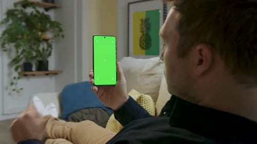 Man holding smartphone in his hands with a green screen, touching the screen as if using it
