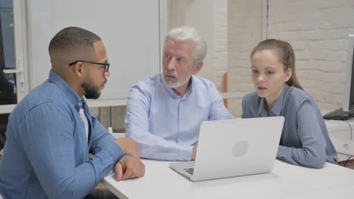 Diverse Team Collaborating Around Laptop in Office