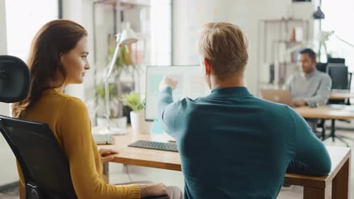 Dois desenvolvedores de software móvel trabalham em computadores desktop e discutem o design de aplicativos para smartphones