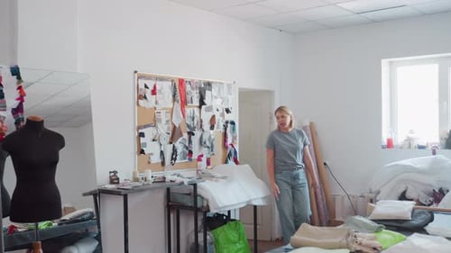 Creative Fashion Designers Entering Workspace with Design Board and Fabric Scattered