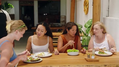 Diverse Young Women Eat Tasty Food Talk with Bipoc Friendly Waiter in Tropical Cafe Asian Caucasian