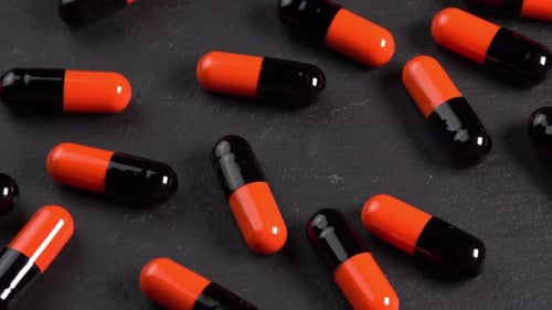 Many black and orange pills capsules or antidepressants rotating on black plate in macro top view