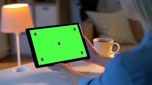 Woman at home video calling on tablet with green screen at night