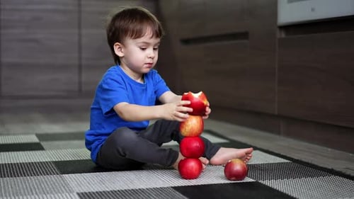 Adorable Caucasian toddler building a tower of red apples.