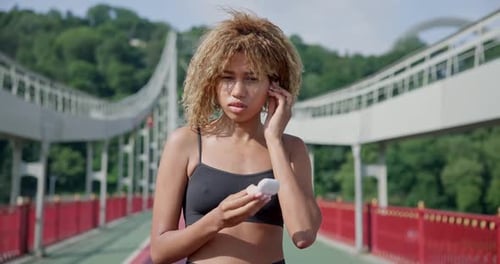 Young African American Woman Putting on Earphones Before Jogging Outdoors on City Bridge
