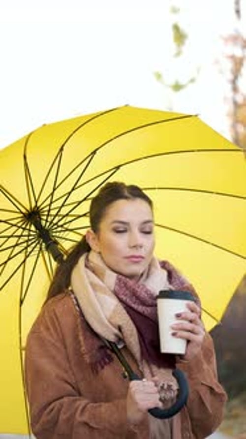 Young Woman Holds Coffee Under Yellow Umbrella in Fall
