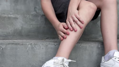 Der Teenager verspürt starke Schmerzen im Knöchel und massiert ein schmerzendes Bein, während er auf Stufen sitzt.