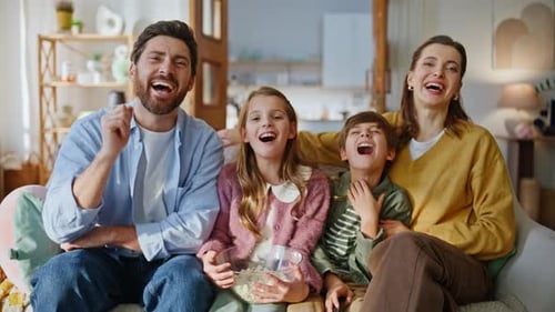 Happy Family Laughing on Couch While Watching TV