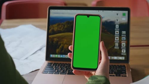 Woman Holding Smartphone with Green Screen Over Laptop