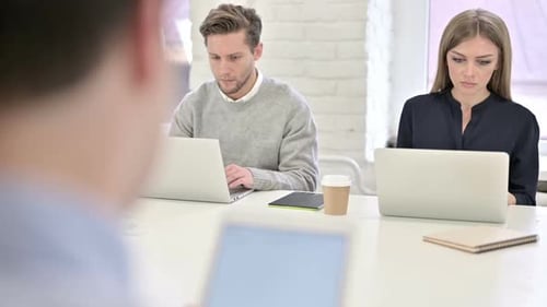 Three Serious Creative Professionals Working on Laptops in Office