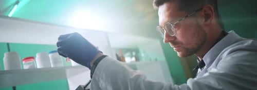 Close Up Scientist Man with Glasses and Protection Gloves Looking Under a Microscope Holding a Tube