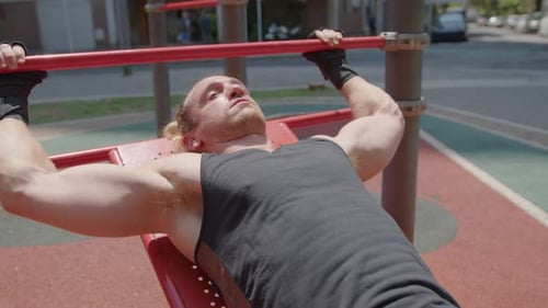 Muscular Man Bench Presses on Outdoor Equipment