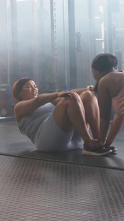Vidéo verticale : faisant des situps assistés, femme en haut gris sur un noyau mat tonifiant, partenaire serrant les pieds