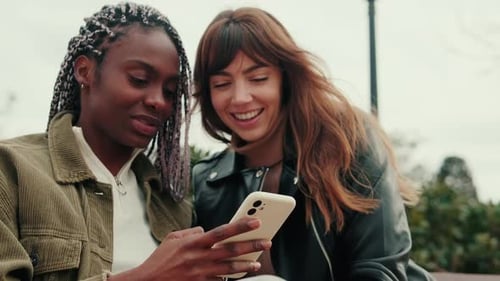 Smiling Women Looking at Phone Together Outdoors