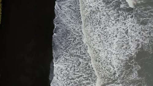 Aerial: Top down aerial view of waves breaking on volcanic black sand beach
