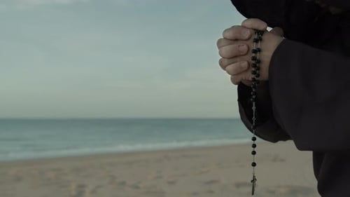 Religious Hands Of A Monk Praying Rosary On The Beach