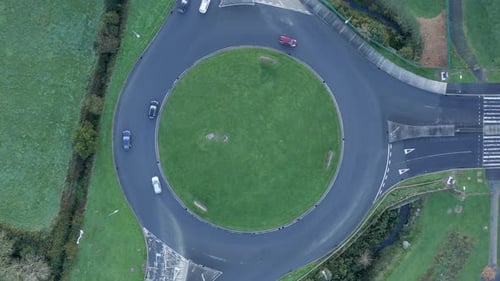 Vehicles drive on green Irish highway roundabout near verdant pastures