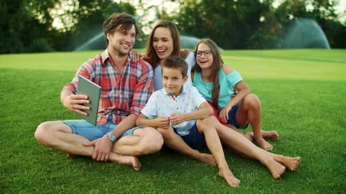 Smiling Family Having Video Chat on Tablet Computer in Meadow. Happy Family