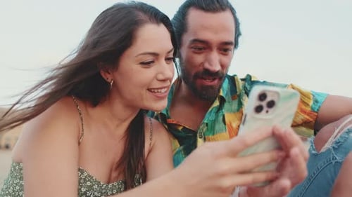 Close-up, young couple using smartphone while sitting on the beach