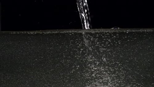 Super-Zeitlupenaufnahme von Spritzwasser gegen schwarzes, ungefiltertes Wasser aus Rohrleitungen mit Sediment
