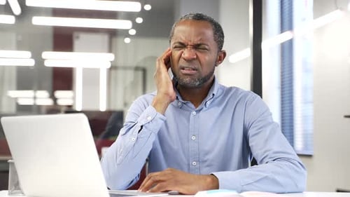 African american businessman suffers from ear pain sitting at workplace in office.