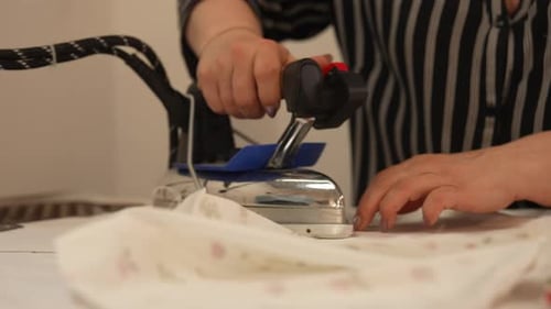 Dressmaker Ironing and Smoothing Floral Fabric with Professional Steam Iron in Textile Workshop