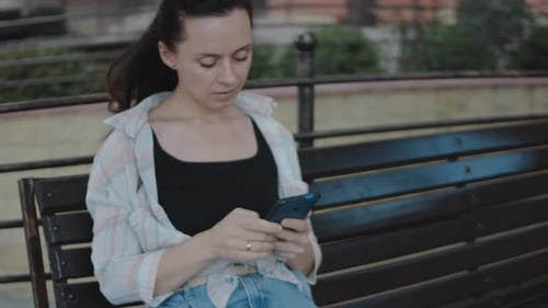 Woman Uses Smartphone While Sitting on Bench