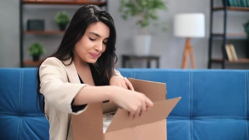 Excited Woman Unboxes Package on Couch at Home