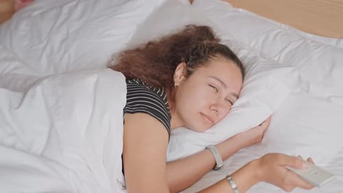 Business Traveler in Hotel Bed Checking Messages Through Sunlight Drowsy Woman Lying in Hotel Room