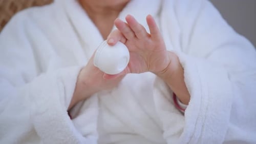 Woman Applies Cream from Container in Close Up